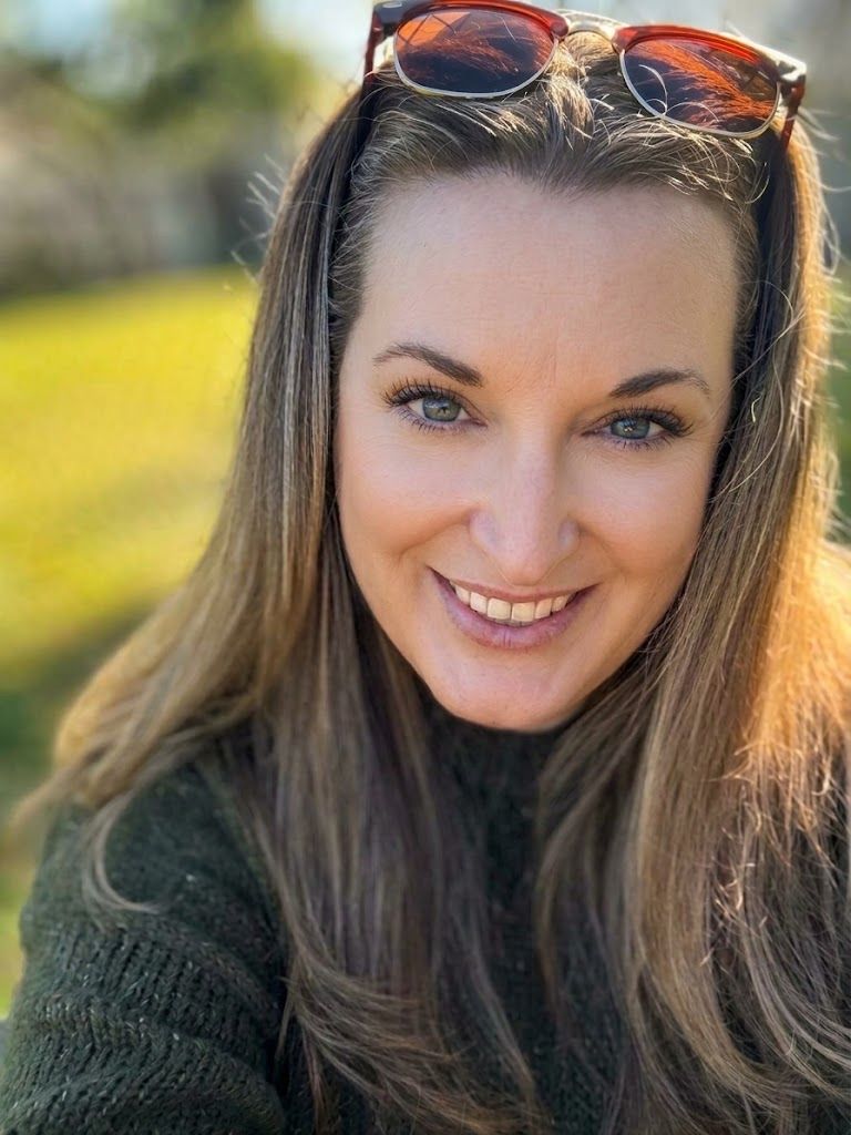 Elyse Schwartz, smiling warmly outdoors in the sun, sunglasses pushed up in her hair